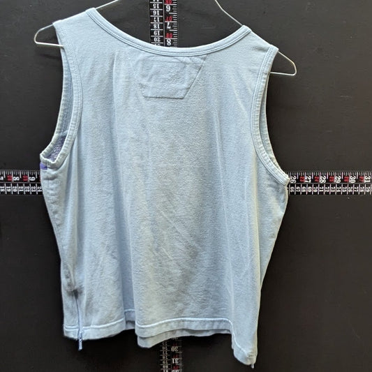 Light blue sleeveless top on a hanger against a dark wall with a ruler below.