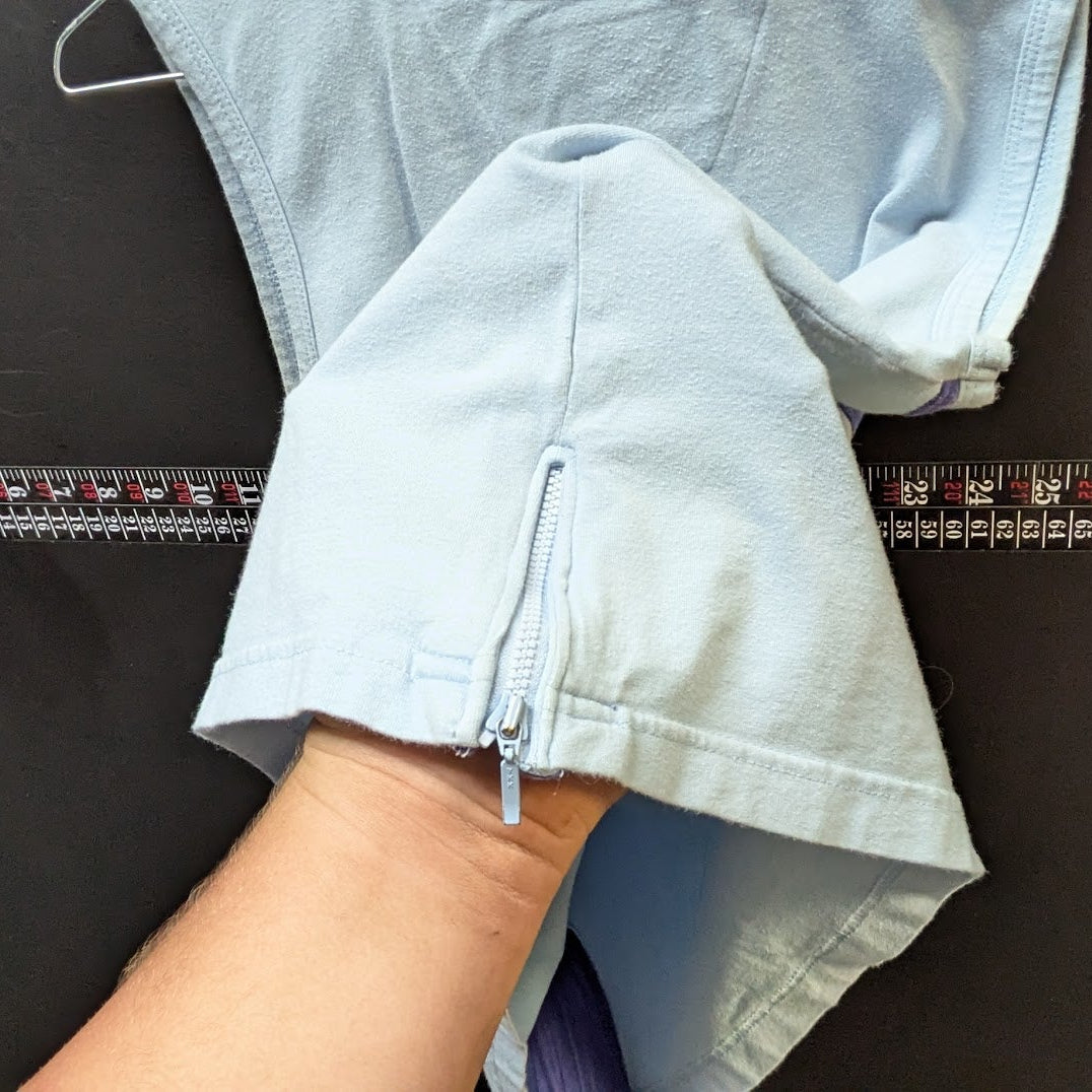 Person holding a light blue jacket with a ruler for scale on a dark surface