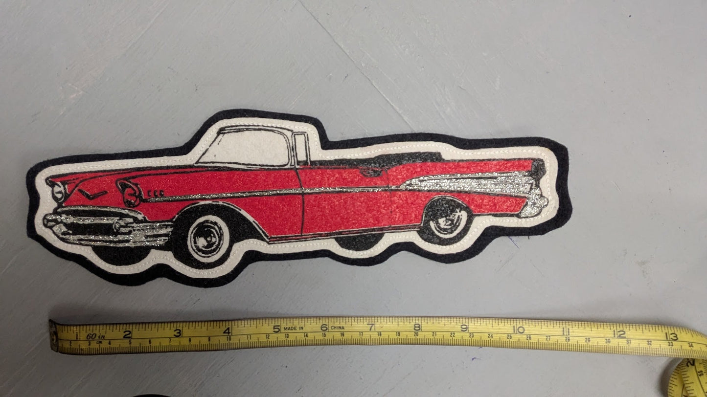 Red and black car-shaped patch next to a measuring tape on a gray surface
