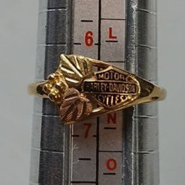 A gold ring with a detailed bee design and textured body, shown on a metal ring sizer held by a hand.
