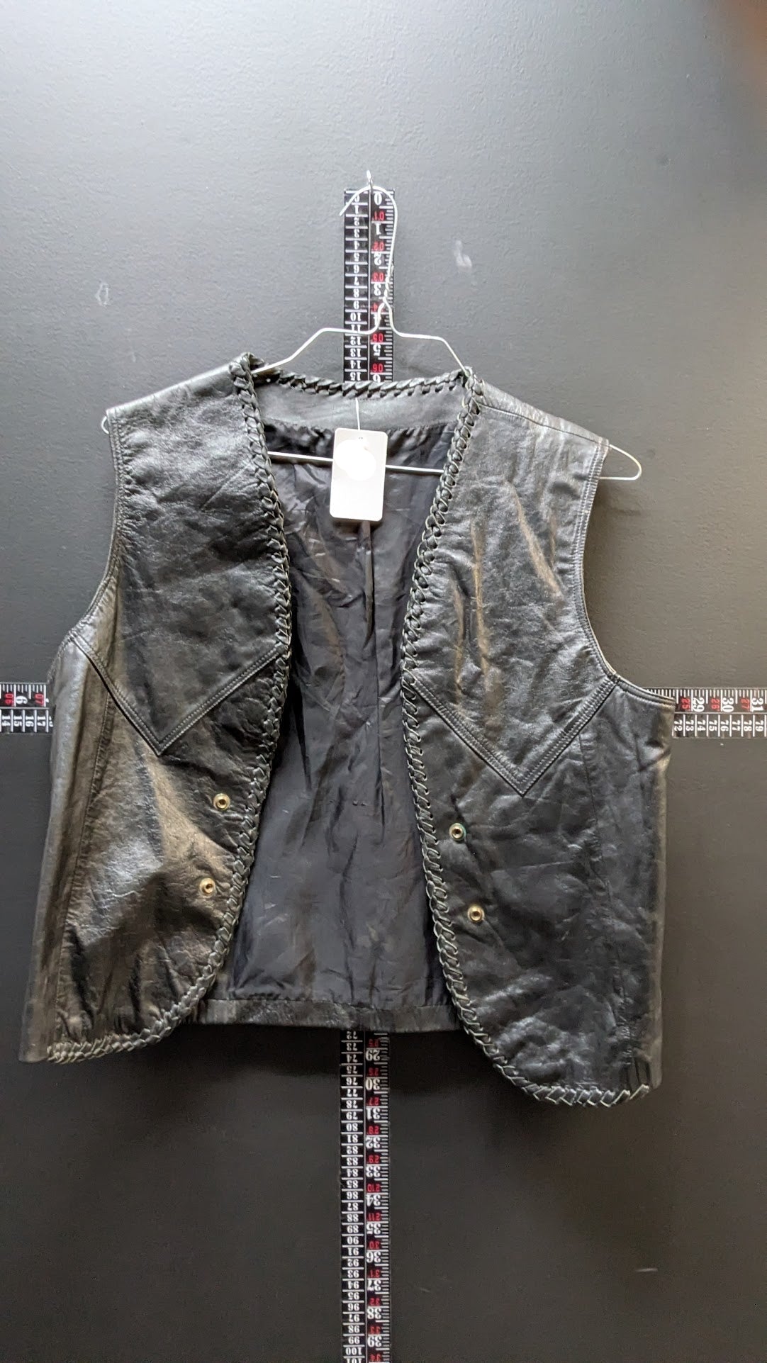 Gray vest on a hanger against a gray wall with a tape measure below.