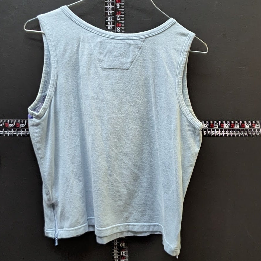 Light blue sleeveless top on a hanger against a dark wall with a ruler below.