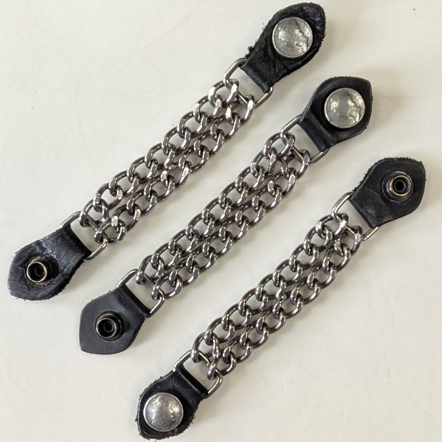 Three black leather straps with metal chain extensions on a checkered background