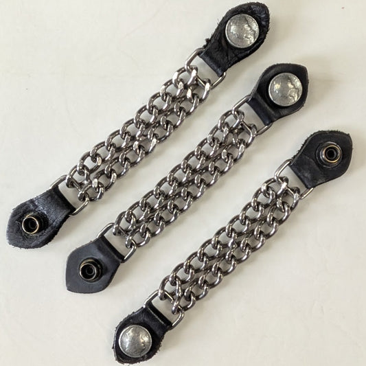 Three black leather straps with metal chain extensions on a checkered background