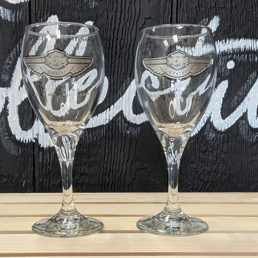 Two wine glasses on a wooden surface with a dark background featuring text.