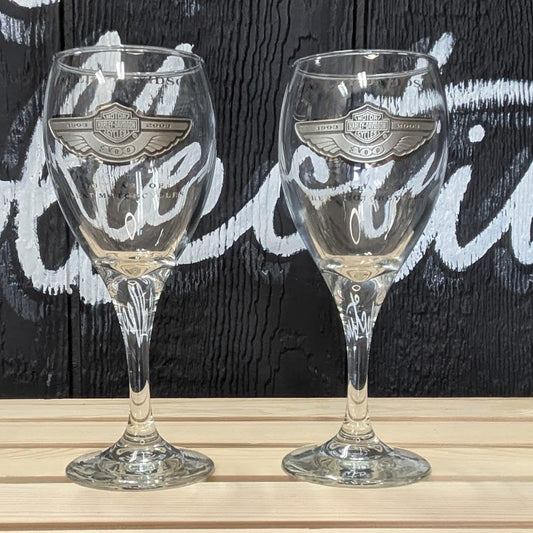 Two wine glasses on a wooden surface with a dark background featuring text.