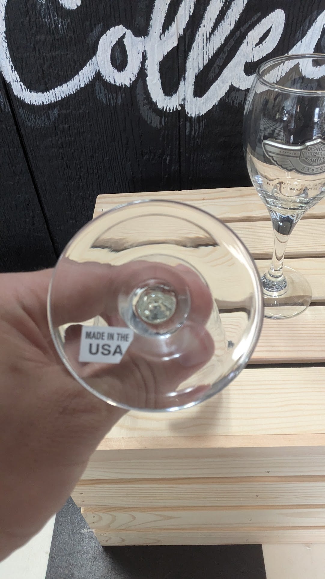 Clear glass with a stem, held by a hand, on a wooden surface with a blurred background.