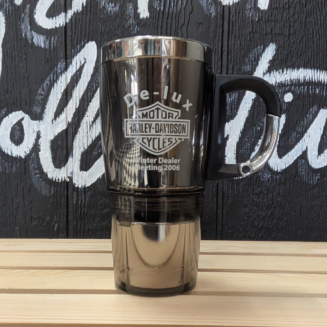 Black and silver travel mug with 'De Lux' branding on a wooden surface with graffiti background.