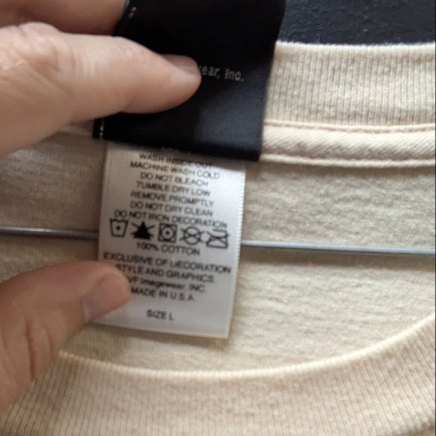 Close-up of a beige garment with a tag and a hand pointing to a label on the fabric.