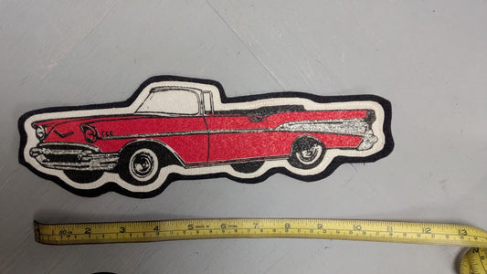 Red and black car-shaped patch next to a measuring tape on a gray surface