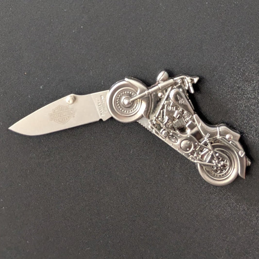A small silver folding pocket knife with a detailed motorcycle handlebar grip design, shown with the blade partially open on a dark gray textured background.