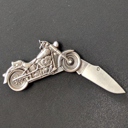 A silver-toned folding pocket knife with a motorcycle design on the blade, resting on a dark gray textured surface.