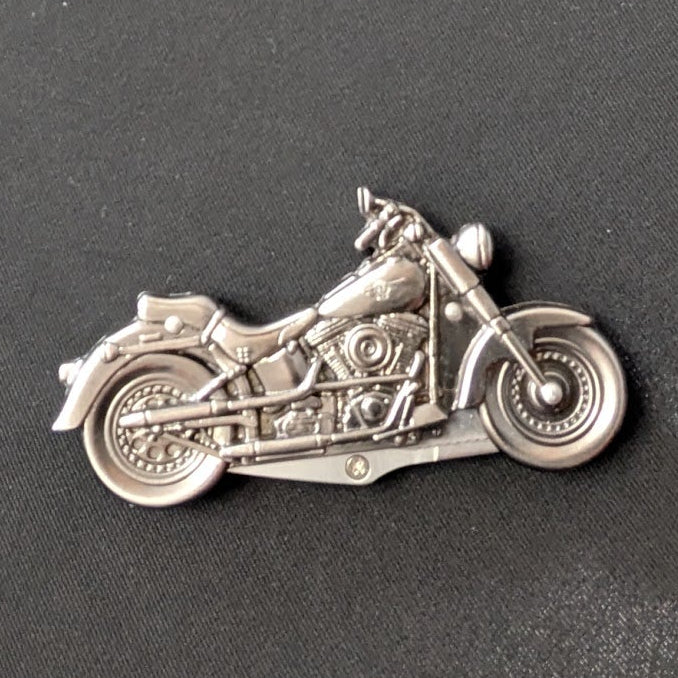 A small silver motorcycle-shaped charm or pin displayed on a dark gray textured surface.