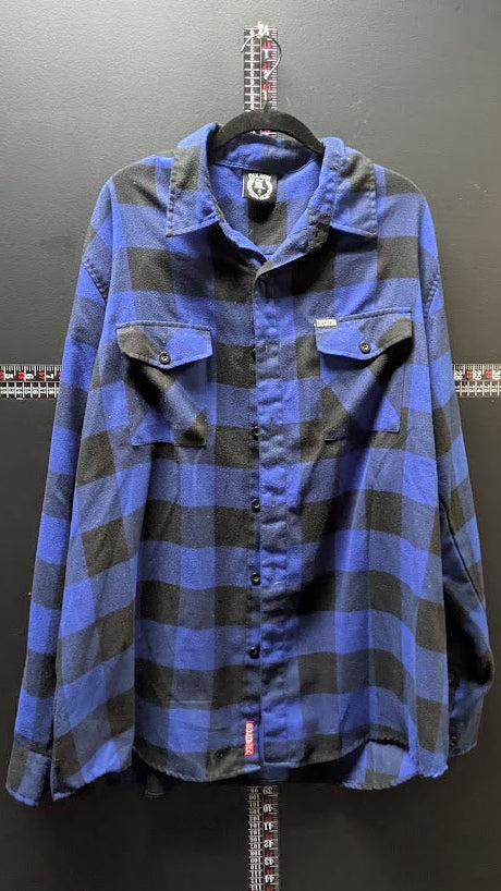 A blue and black plaid long-sleeve button-up shirt hanging on a black hanger against a dark gray wall, with a small red tag near the lower hem.