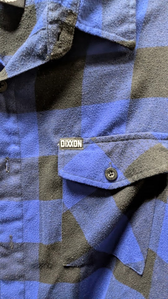 Close-up of a blue and brown plaid flannel shirt with a chest pocket and a visible Dixon brand label.