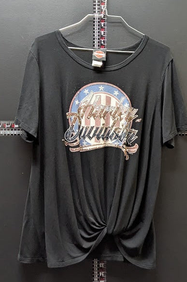 A black short-sleeve t-shirt with a distressed graphic on the front reading 'Merry Brunch' in a patriotic red, white, and blue circular design. The shirt is styled with a front twist detail and hangs on a hanger against a dark gray wall.