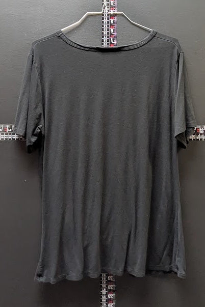 A dark gray short-sleeve t-shirt hanging on a metal hanger against a dark gray wall, with a measuring tape visible behind it.