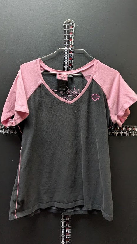 A women's short-sleeve raglan t-shirt hanging on a metal hanger against a dark gray wall. The shirt features a dark charcoal gray body and light pink sleeves, with a small pink embroidered logo on the left chest.