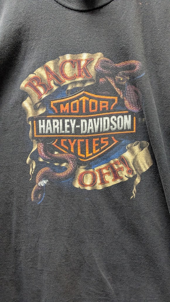 Close-up of a dark gray heather graphic t-shirt featuring the retro Harley-Davidson 'Back Motor Cycles Off!' logo with snakes and a bar-and-shield design.