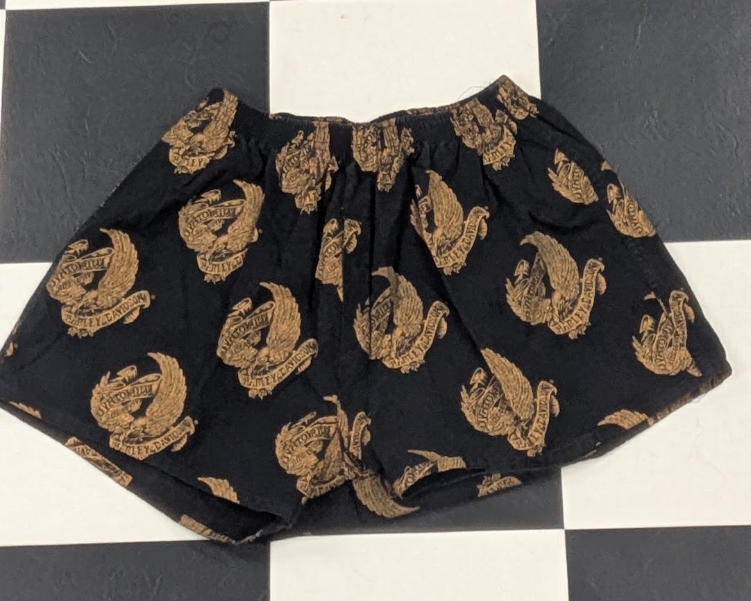 Black shorts with a repeating gold dragon pattern, laid flat on a black and white checkered floor.