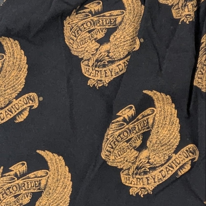Black boxer briefs with an all-over gold eagle crest print, laid flat on a dark textured surface.
