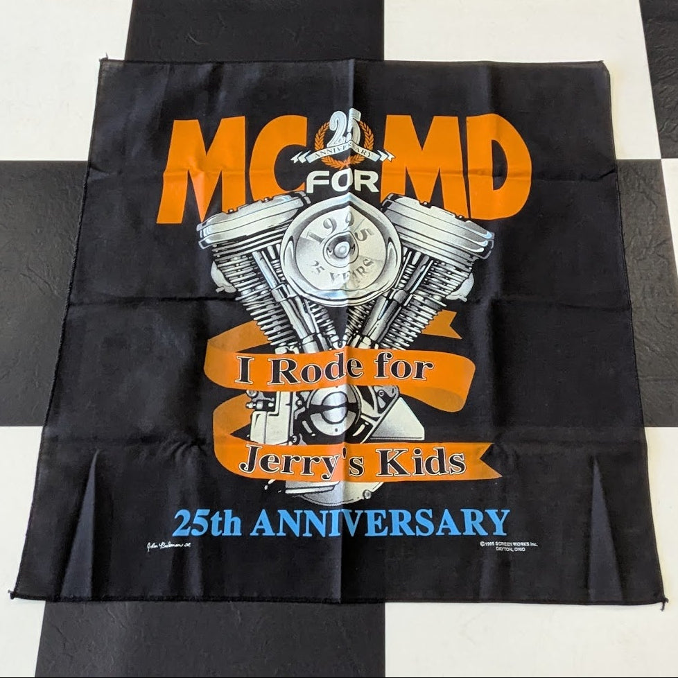 A black fabric flag or banner laid flat on a black and white checkered floor. The banner features a graphic of a motorcycle engine with the text 'MC MD FOR I Ride for Jerry's Kids' and '25th Anniversary' in orange, white, and blue lettering.