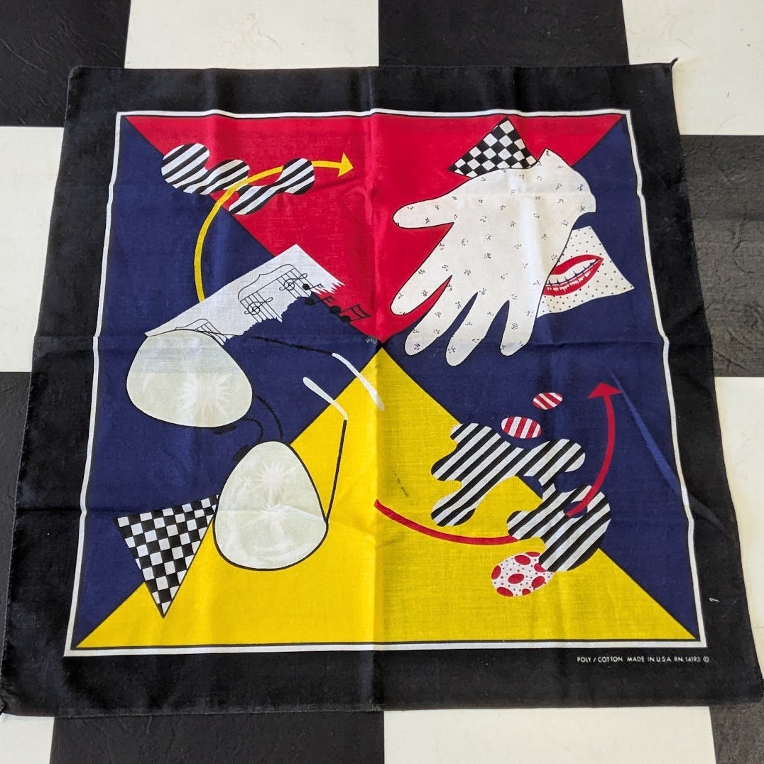 A square vintage-style scarf laid flat on a black and white checkered floor. The scarf features a bold abstract design with a navy blue background, a red triangle, a yellow triangle, a white glove, striped black-and-white shapes, and small red lips near the top right.