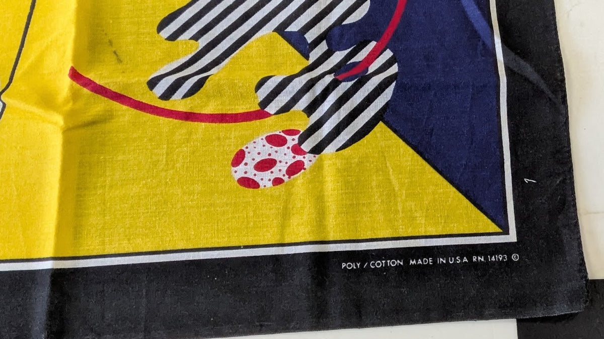 A close-up of a vintage cotton textile, likely a tablecloth or napkin, featuring a bold mid-century modern graphic design. The design includes a yellow background, a navy blue geometric shape, black-and-white striped legs, and a red-and-white patterned soccer ball.
